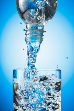 Clear drinking water pouring into a tall glass from a transparent plastic bottle.