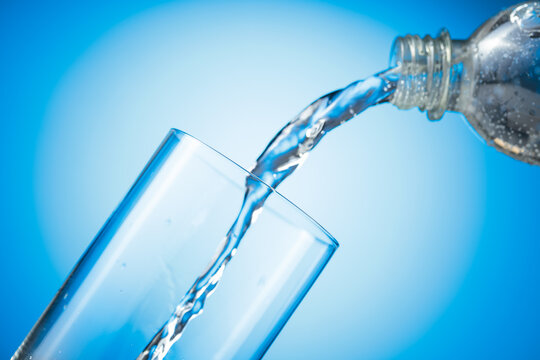 Clear drinking carbonated water pouring into a tall glass from a transparent plastic bottle.