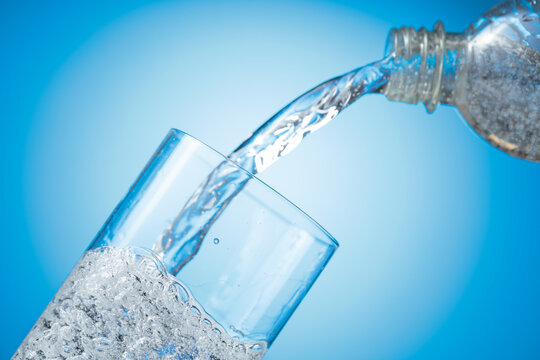 Clear drinking carbonated water pouring into a tall glass from a transparent plastic bottle.