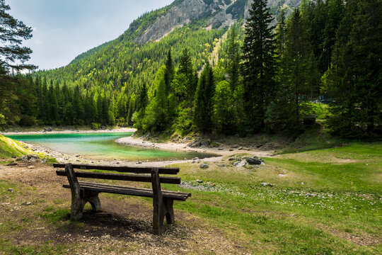 Wooden bench overlooking the Gruner See in Austria surrounded by mountain and forest, illustrating seasonal water level decline.