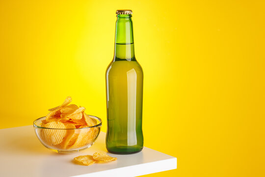 Beer bottle and chips on yellow background snack setup