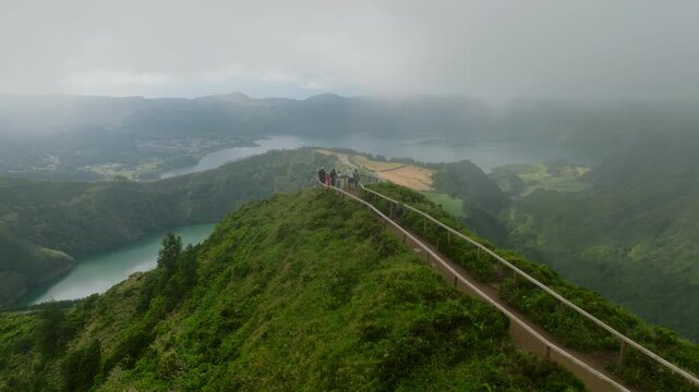 Aerial view of the Boca do Inferno viewpoint, featuring a narrow ridge path overlooking the stunning Sete Cidades volcanic crater lakes surrounded by steep, mist-covered green slopes, S&atilde;o Miguel