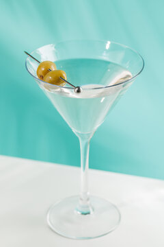 Classic martini cocktail with olives in glass on blue background