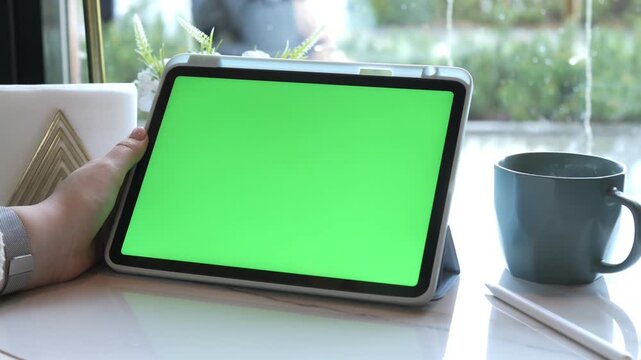 Person holds tablet with green screen near window. Coffee cup and notebook sit beside. Calm, focused atmosphere for work or presentations. Ideal for digital content, tutorials, or marketing mockups