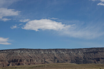Obraz premium Wide desert mesa landscape beneath expansive blue sky and soft white clouds in remote arid wilderness.
