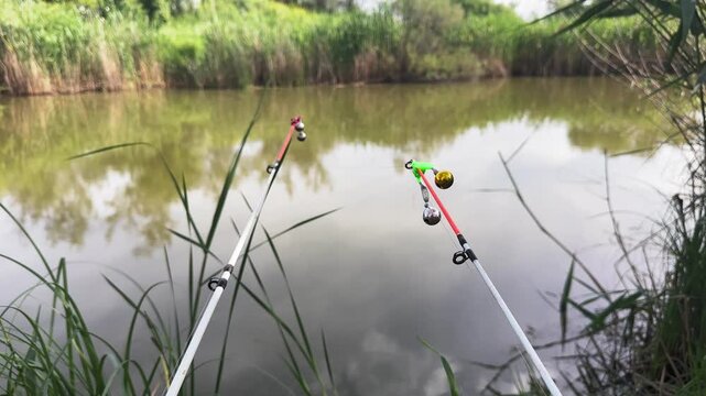 Fishing rods with bell indicators waiting for fish bite near lake shore. Concept of recreational fishing and outdoor relaxation.