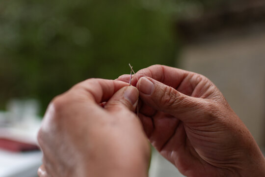 Senior woman threading needle with white thread close up