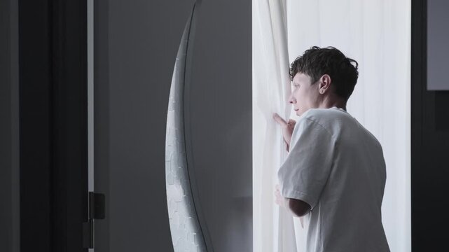 Paranoia and persecution mania concept with anxious man secretly looking through curtain, psychological fear, surveillance suspicion and unsafe home atmosphere