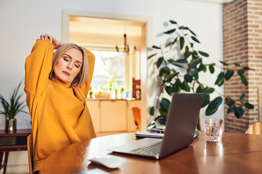 Woman stretching neck and back while working at laptop at home