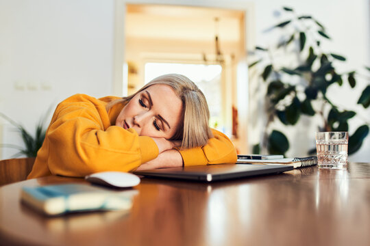 Tired woman napping at desk with laptop at home
