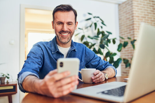 Man smiling using smartphone and laptop at home
