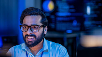 Obraz premium Focused Indian technology professional pointing at an office computer monitor to debug core processor microchip script data and hardware memory logic.