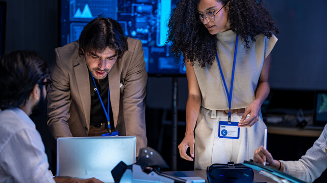 A multiethnic technology developer team holding and inspecting a raw silicon wafer disk to check semiconductor circuit microchip fabrication logic parameters in a workspace.