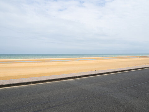 Paisaje de la playa de Omaha Beach en la costa normanda francesa, con diferentes colores y texturas, cielo nuboso, arena dorada, mar azul, carretera oscura. 2022