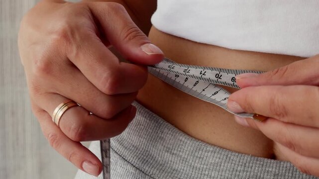 Woman measuring waist with tape measure for fitness progress, weight loss and healthy lifestyle.