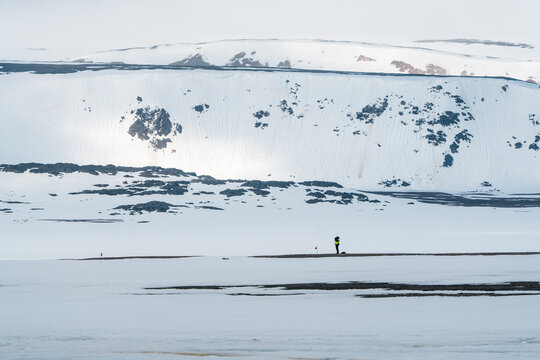 Svalbard, Svalbard and Jan Mayen - 24 April 2026: View of a person with a backpack standing in a vast snowy arctic landscape with mountains and rocky outcrops.