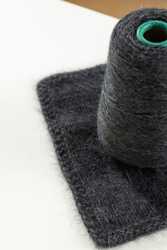 Dark gray premium wool yarn cone and knitted swatch on white tabletop for yarn shop and craft supply advertising