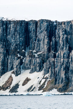 View of the towering basalt cliffs of Alkefjellet with nesting seabirds and snow-covered slopes above the sea in Svalbard, Svalbard and Jan Mayen.