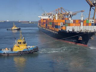 Fototapeta premium unmooring container ship full of containers. two tug boats pull, lay out this vessel off berth. water seethe near the tugs, lines tight.