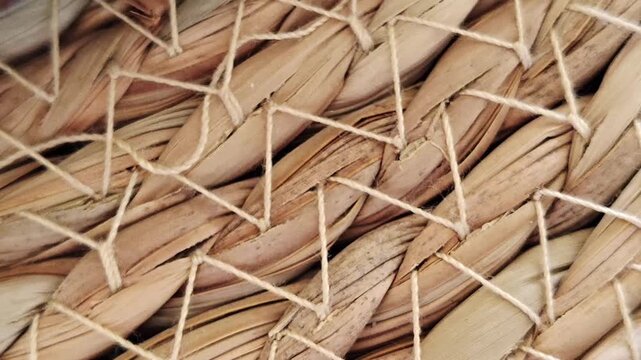 Video in smooth panning motion; close-up of woven natural fiber texture with braided strands and zigzag stitching securing the weave