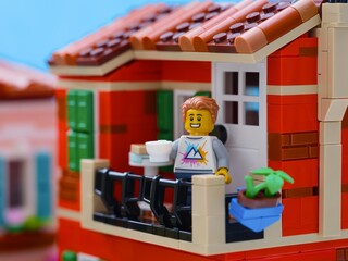 Obraz premium Tambov, Russian Federation - January 04, 2026 Lego man minifigure with a white cup standing on a balcony in a Mediterranean city.