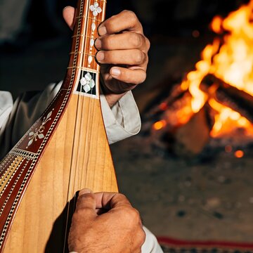Close up of rural hands playing traditional Afghan rubab by campfire light during a wedding, copy space