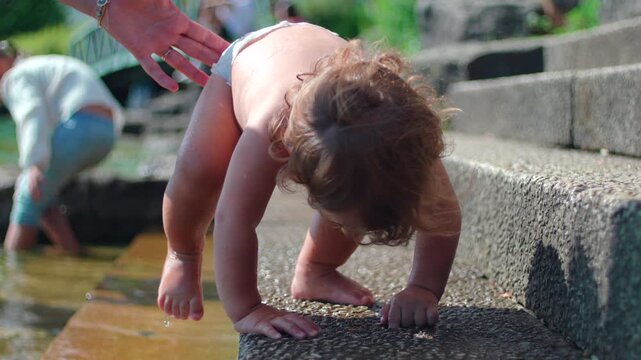 Toddler inspecting small hole on wet lakeside step during summer outing capturing curiosity, sensory discovery and authentic childhood exploration outdoors