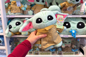 Naklejka premium Dubai, UAE - 24 may 2026: Grogu plush toy from Star Wars franchise held inside retail store with multiple character dolls on shelves, highlighting pop culture merchandise and fan shopping trend