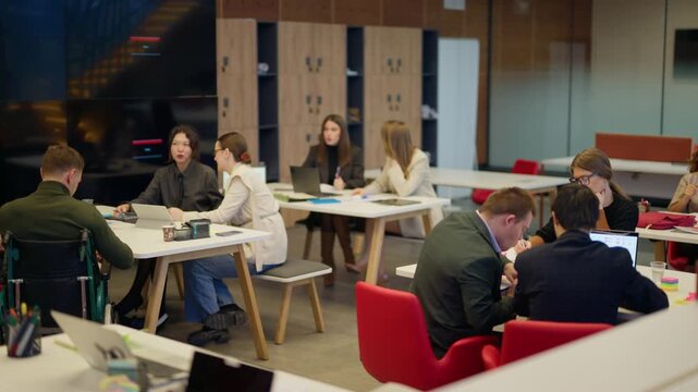 A diverse group of professionals are engaged in collaborative work within a modern office setting. Team members are focused on their tasks, utilizing laptops and engaging in discussions.