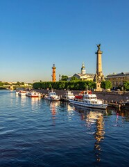 Fototapeta premium Historic Riverside Promenade with Moored Boats and Tall Monument Under Clear Blue Sky