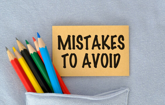 Colorful pencils lean near a sticky note. Note reads MISTAKES TO AVOID in bold black letters. Note rests in a folded fabric pocket.
