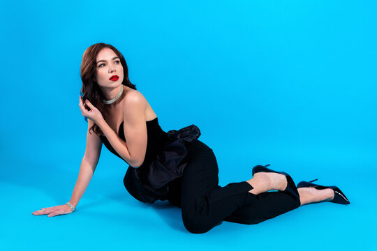 Elegant fashion model in black evening wear and diamond jewelry posing on a vibrant blue studio background, glamour portrait and stylish beauty concept