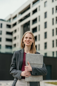 Elegant business professional woman holding laptop outside modern building