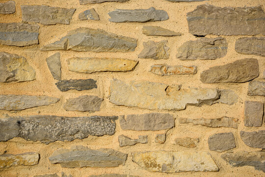 Old traditional stone wall background texture with rustic irregular rocks and yellow mortar ideal for architectural and construction design backdrops