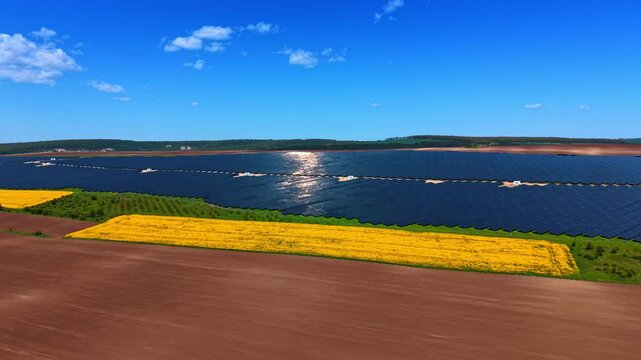 Brown, yellow and green fields around the photovoltaic cell site. Multiple solar panels sparkle in the sun. Drone footage.