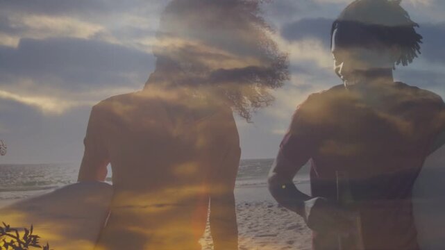 Two adults facing ocean at sunset walking along shore carrying boards lifting drink clouds blending