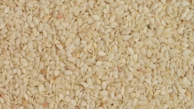 A top down, close-up shot of white sesame seeds slowly rotating. Perfect for topics related to healthy eating, vegan food, agriculture and organic ingredients.