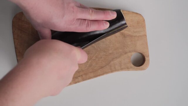 Hands slicing a fresh eggplant lengthwise on a wooden cutting board