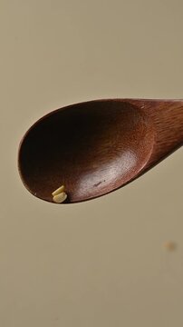 Dry yellow split dry peas gently falling from a wooden spoon against a neutral beige background. High quality close-up shot for culinary, cooking, and healthy nutrition concepts