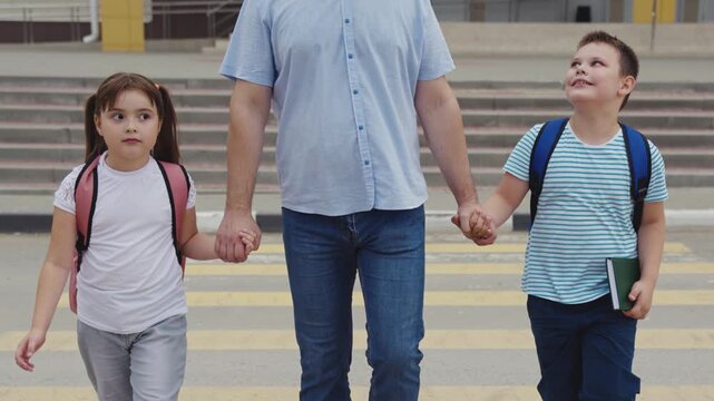 Children escorted by parent, School backpacks visible, Road safety in action, Father s loving care, Start of school day, Peaceful morning walk, Sidewalk to school, Childhood memories, Important road