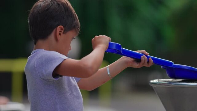 Boy compacting sand inside playground funnel with blue shovel during outdoor playtime capturing concentration, experimentation and authentic childhood learning