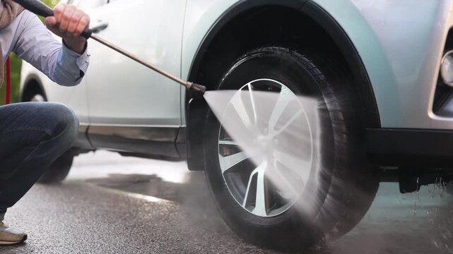A person is pressure washing a car wheel and tire with a high-pressure water jet, cleaning away dirt and grime