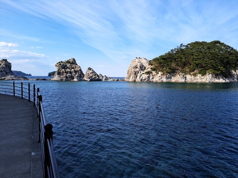 青空と澄んだ海に佇む白い巨岩と海岸の遊歩道