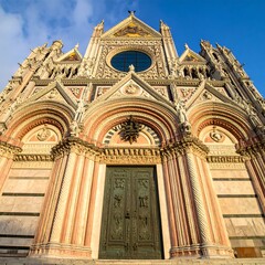 Naklejka premium Ornate Gothic Cathedral Facade Rising Under Clear Blue Sky in Historic Italian City
