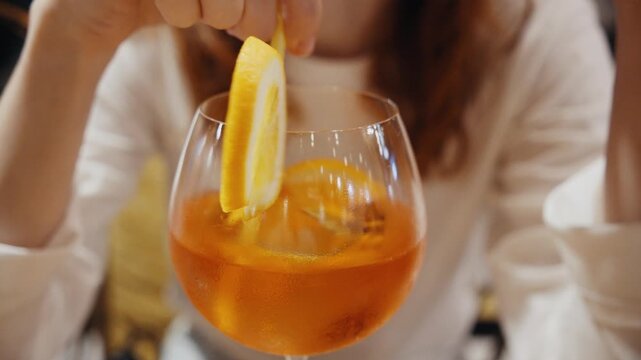Woman stirring aperol spritz cocktail with a straw