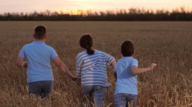 Happy cheerful children hold hands, run across field. Jolly joyous children kids playing together running around field, holding hands. Merry children siblings kids family rush together across field.