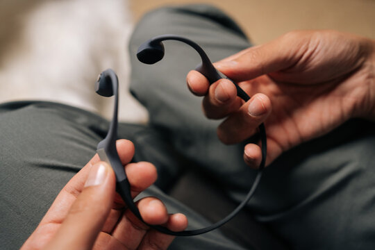 Cropped shot of male hands holding bone-conduction headphones, preparing to listen to music or audiobook outdoors while engaging in activities, offering open-ear listening experience, close-up.