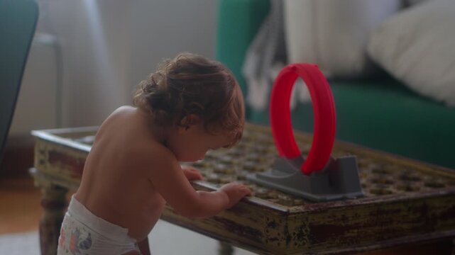 Toddler dropping toy car through holes in rustic coffee table during morning play at home exploring gravity and cause and effect