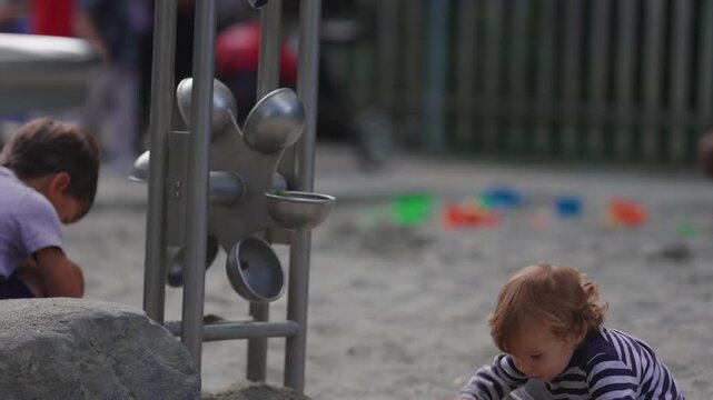 Toddler falling backward into sandbox during playground play capturing imbalance, movement and authentic outdoor childhood learning experience