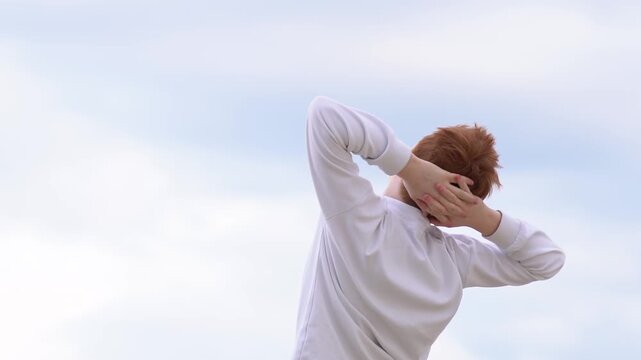A relaxed teenage boy breathes in the fresh air with his hands behind his head, basking in the sun. Dreams, freedom, and the concept of travel. High quality FullHD footage